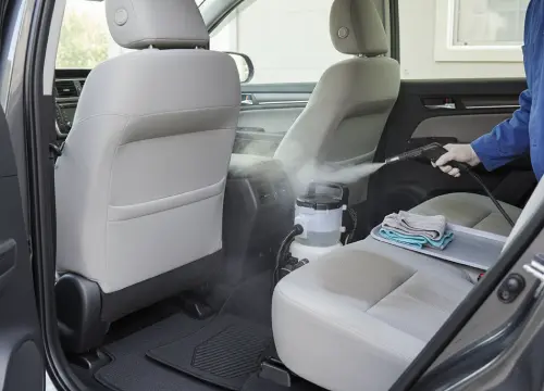 Detailer shampooing and steam-cleaning car seats and carpets with extraction tools