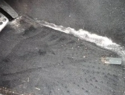 Gloved hands wiping salt stains from car carpet.