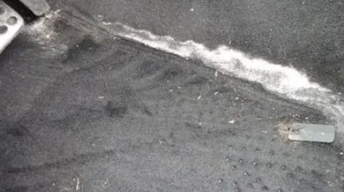 Gloved hands wiping salt stains from car carpet.