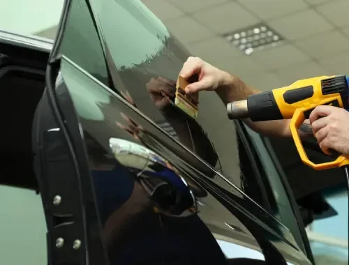 Technician measuring glass before applying window film to a parked car.