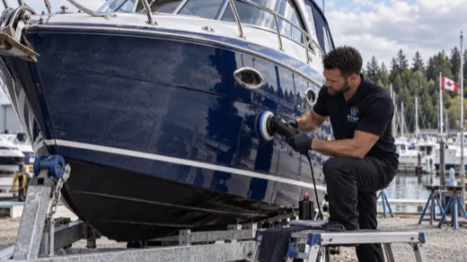 WhipWashPro technician polishing the hull of a dark blue cabin cruiser