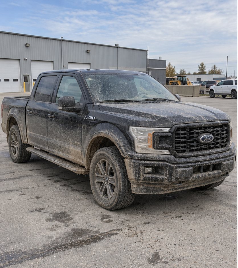 Black Ford F-150 pickup truck front end heavily coated in dried mud