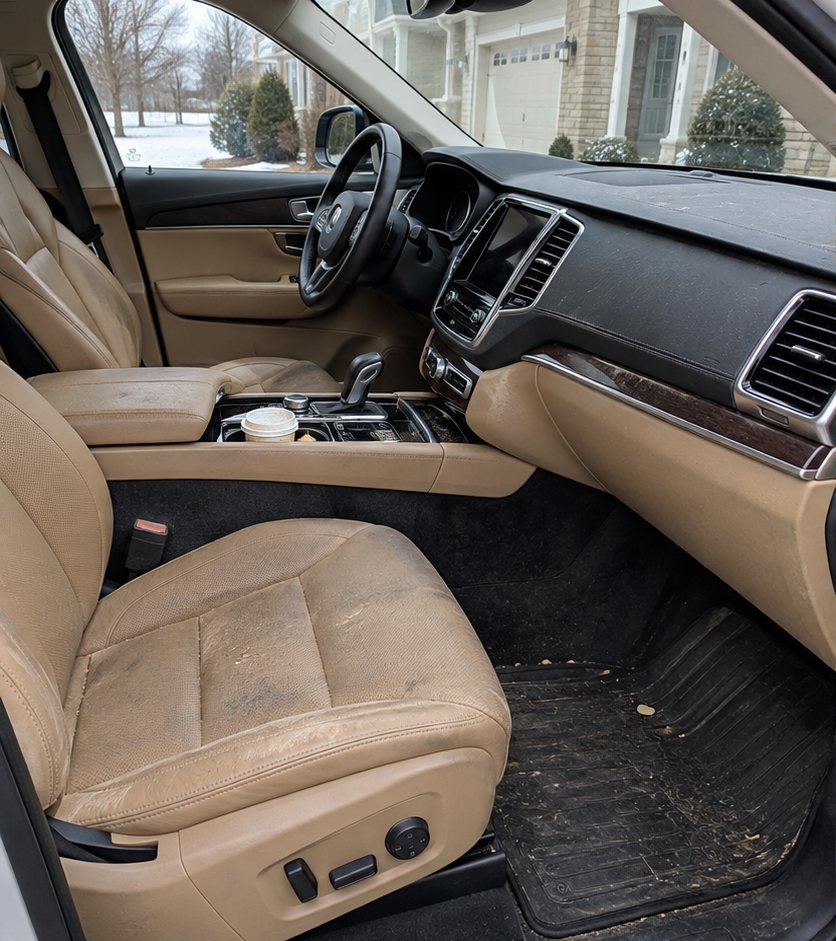 Tan leather SUV front seat and dashboard with visible dust, wear marks and a used coffee cup in the console